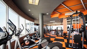Une salle de sport équipée de divers appareils d’exercice, dotée de grandes fenêtres et d’un sol à carreaux.