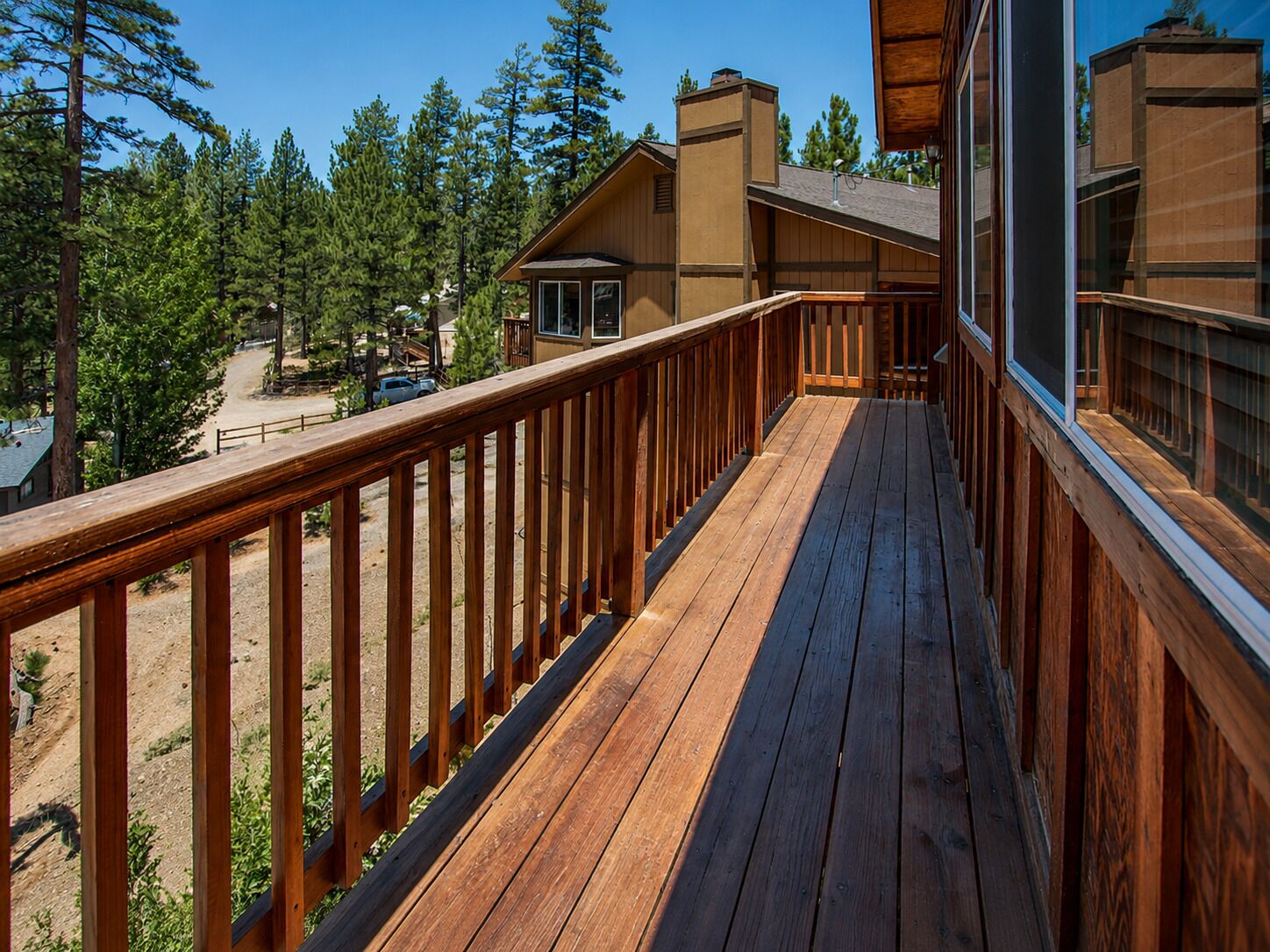 A wooden deck with a railing, overlooking a forested area with buildings in the background.