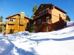 A wooden cabin with a balcony and a staircase leading to the upper floor, surrounded by snow.