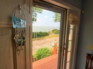 Una puerta de madera con un letrero que dice 'WELCOME', una puerta de cristal que da a una terraza con vista al mar y una barrera de cuerda.