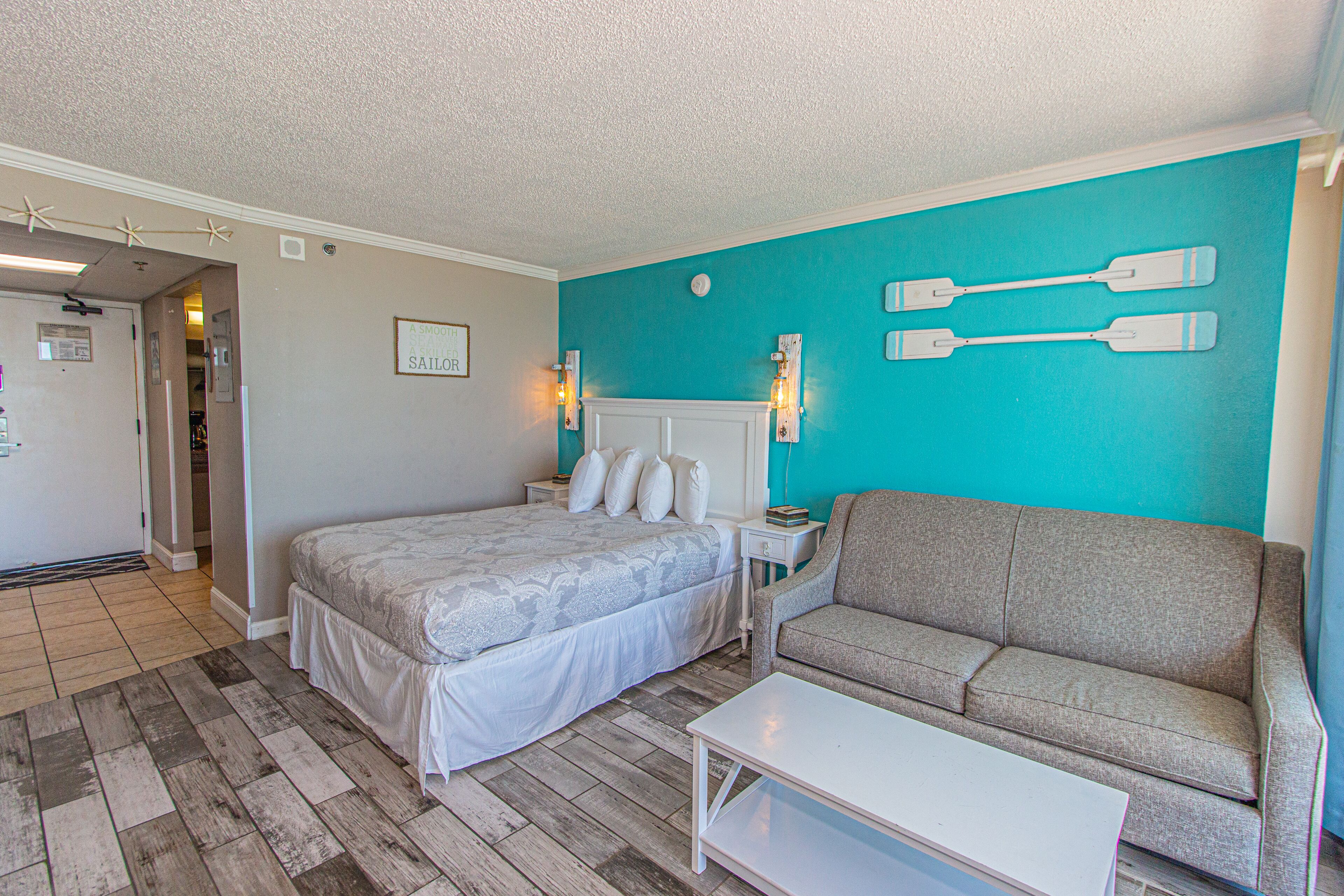 A bedroom with a bed, a sofa, a nightstand, and a wall-mounted light fixture.