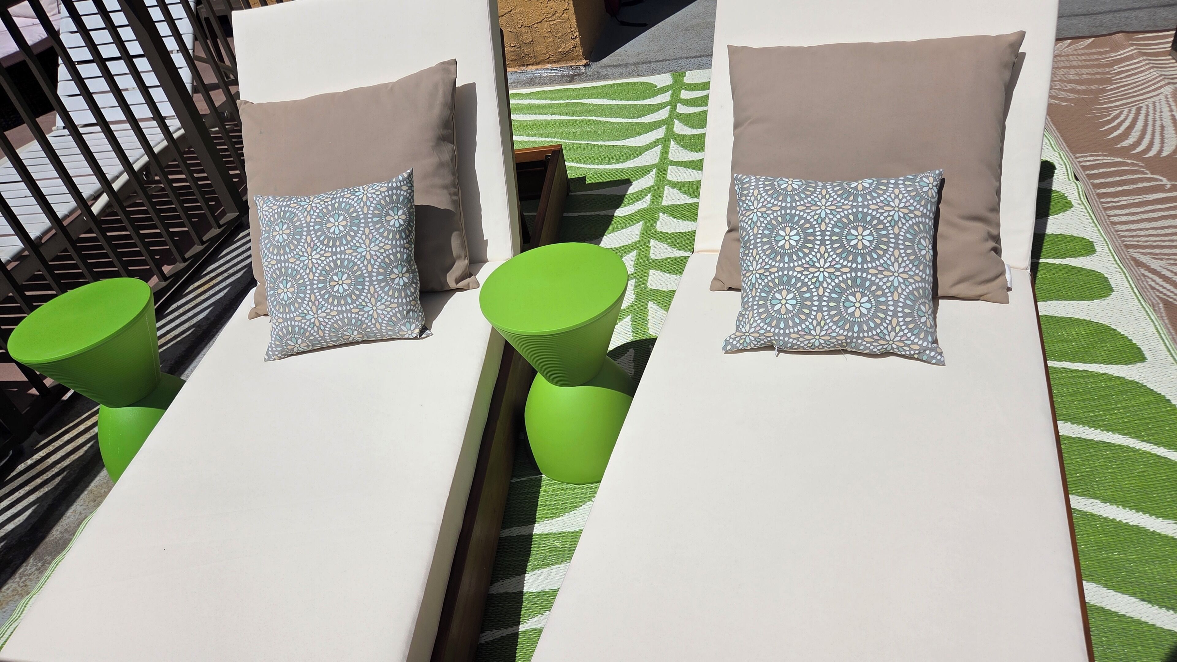 A sunbed with a patterned pillow, a green stool, and a patterned rug.