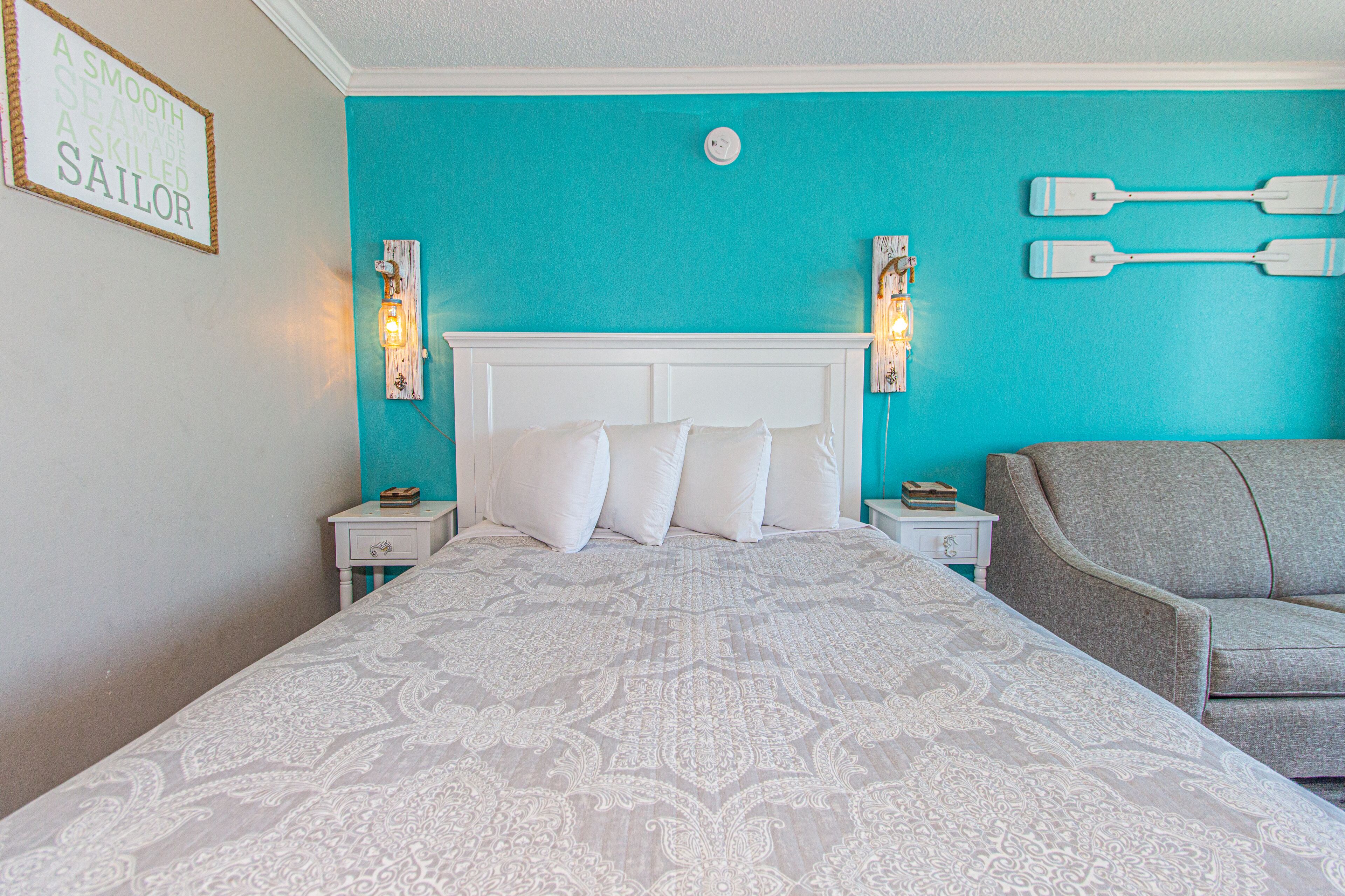 A bedroom with a bed, two nightstands, a chair, and a wall with a sign and two wall-mounted lights.