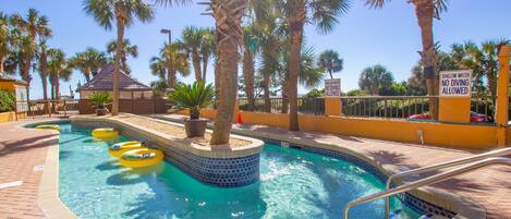 A pool area with a shallow water sign, a 2 FT no diving sign, and palm trees around.