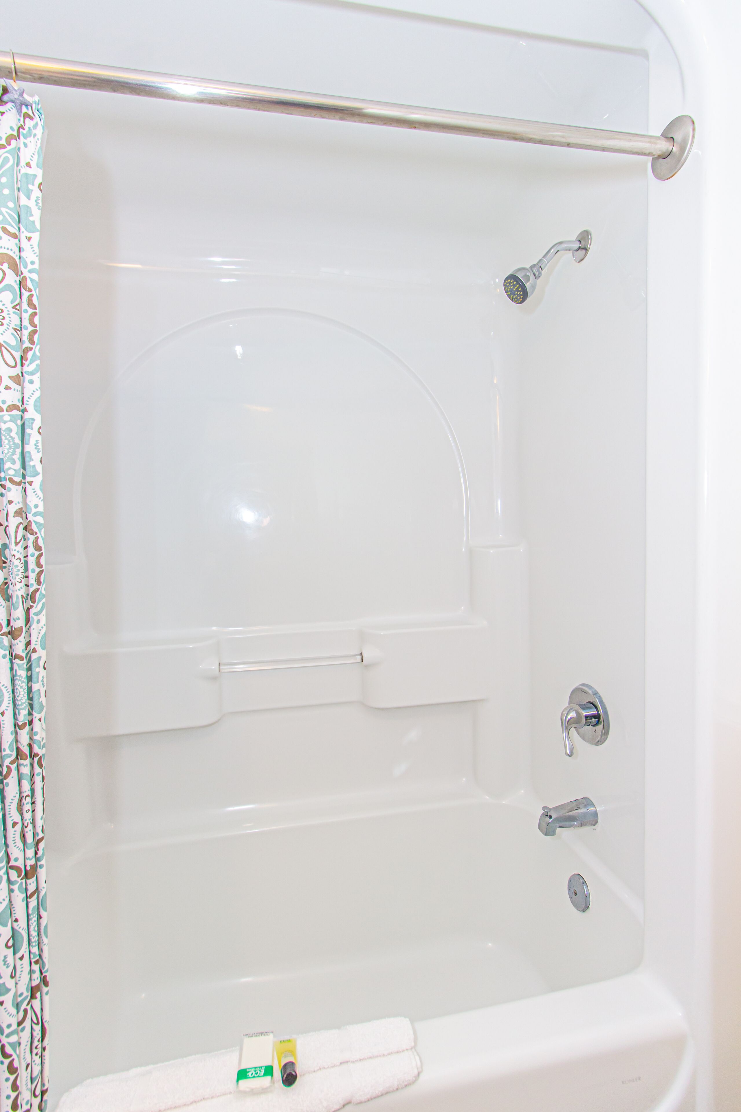 A white bathtub with a shower curtain, a handheld showerhead, and a grab bar.