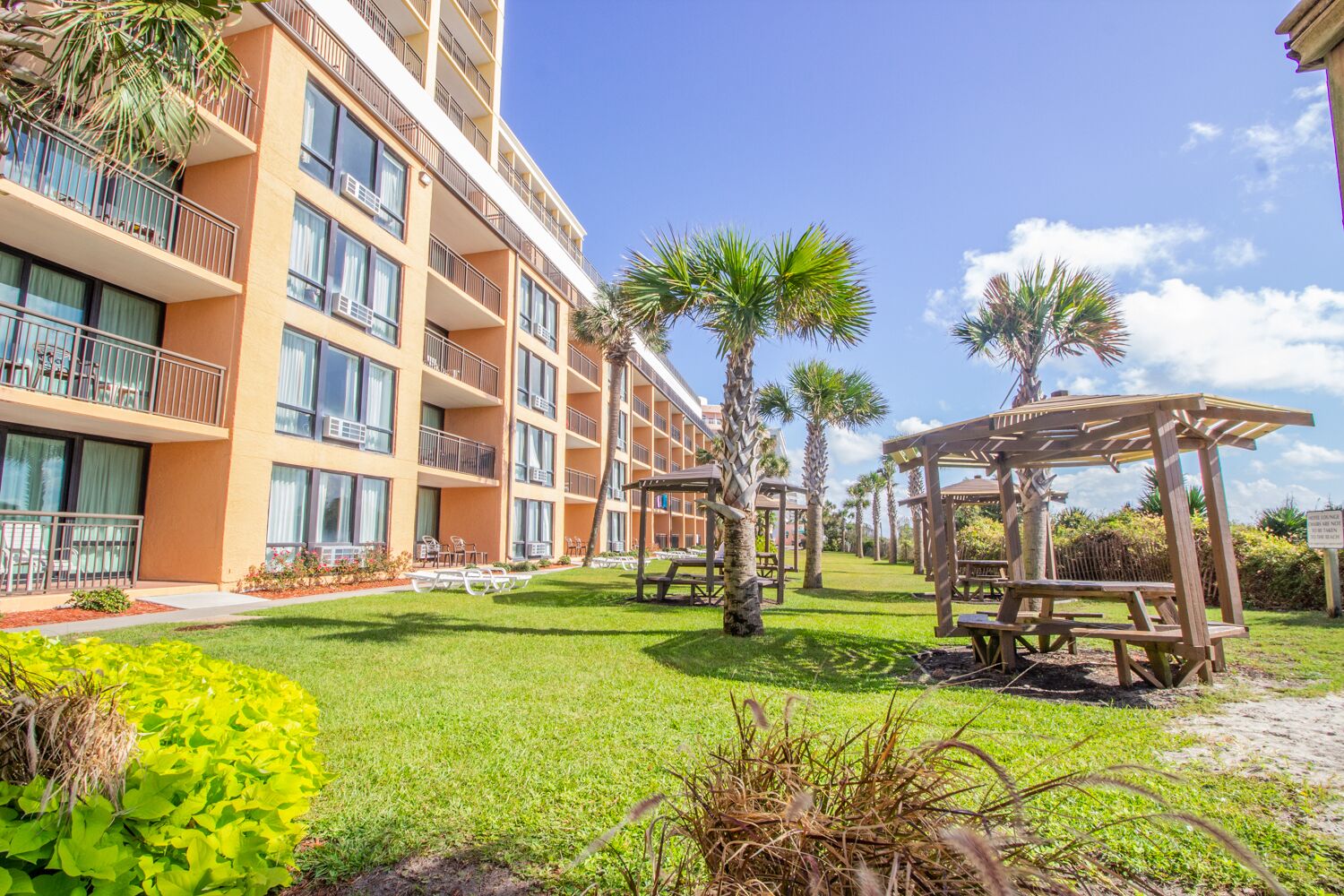 A multi-story hotel with balconies, outdoor seating areas, and palm trees.