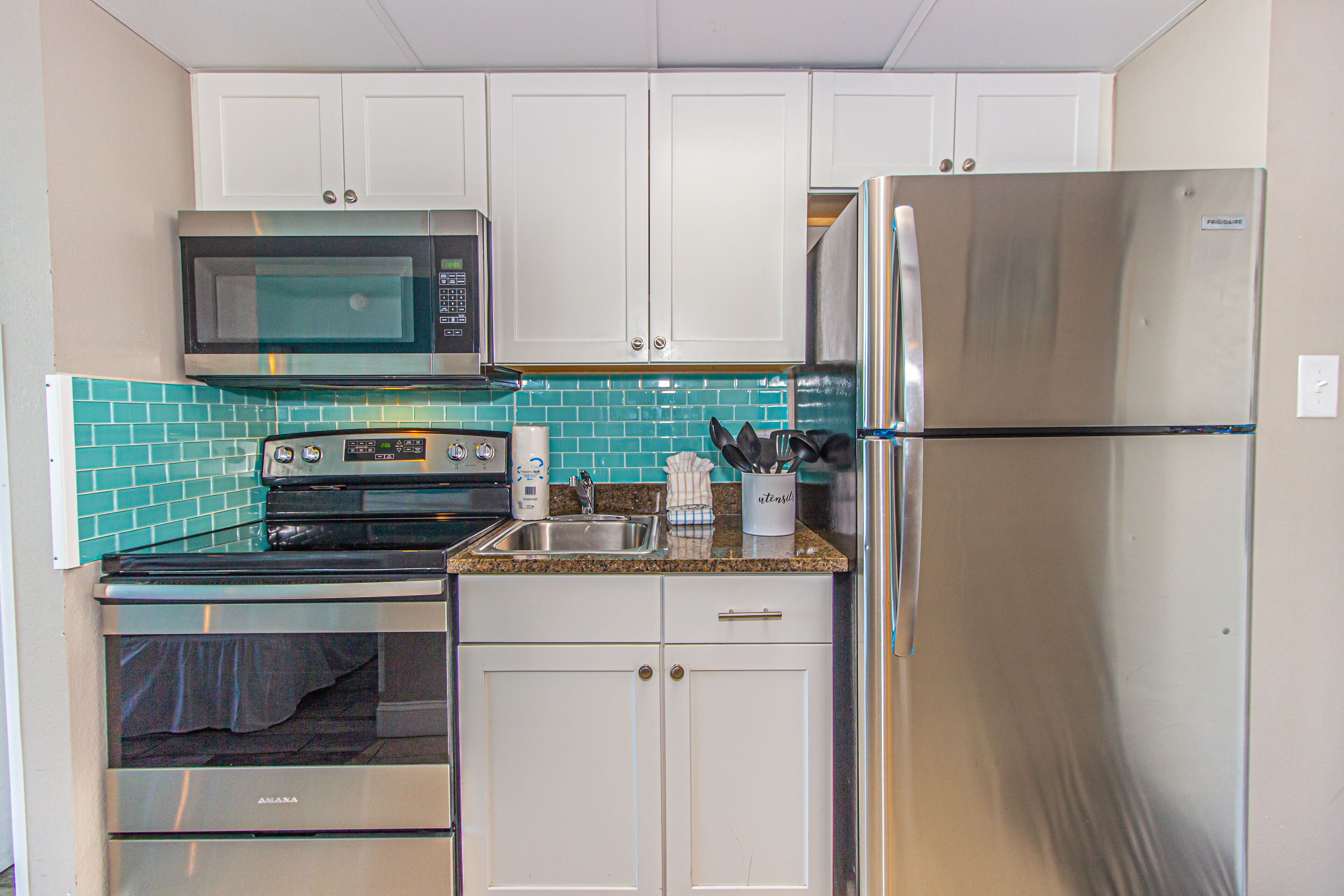 A compact kitchen with white cabinets, a stainless steel refrigerator, a microwave, and a stove.