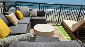 A balcony with a sofa, cushions, a round table, and a chair. - Over-sized Luxury Balcony with teak loungers! Modern Style in the Golden Mile (Myrtle Beach)