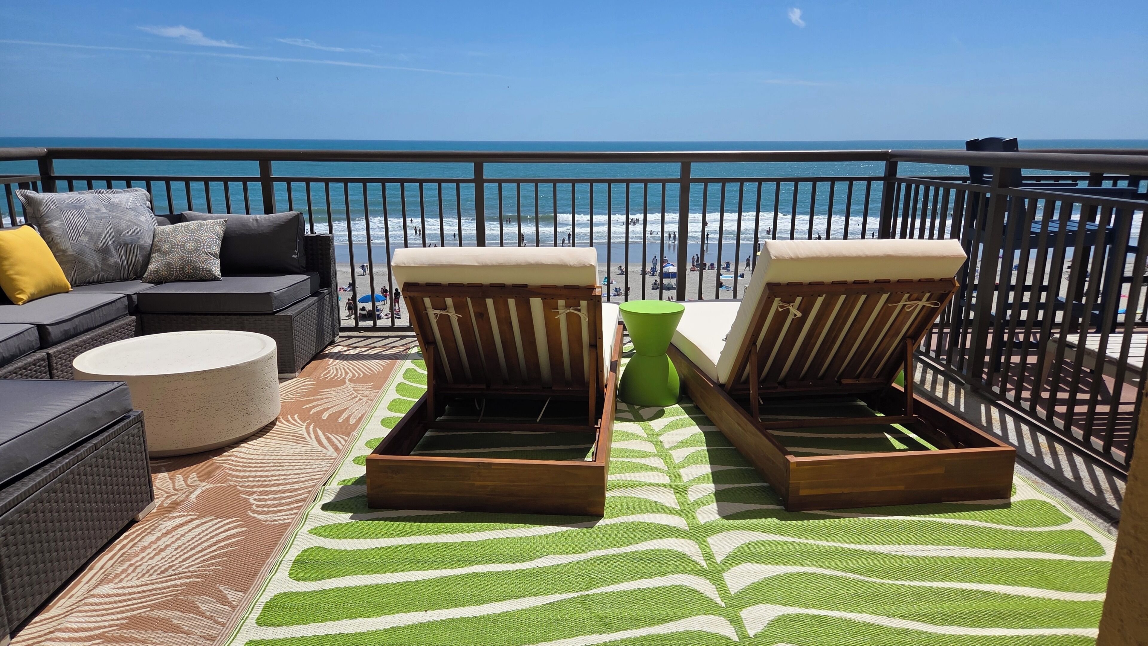 A balcony with a sofa, two lounge chairs, a round table, and a patterned rug.