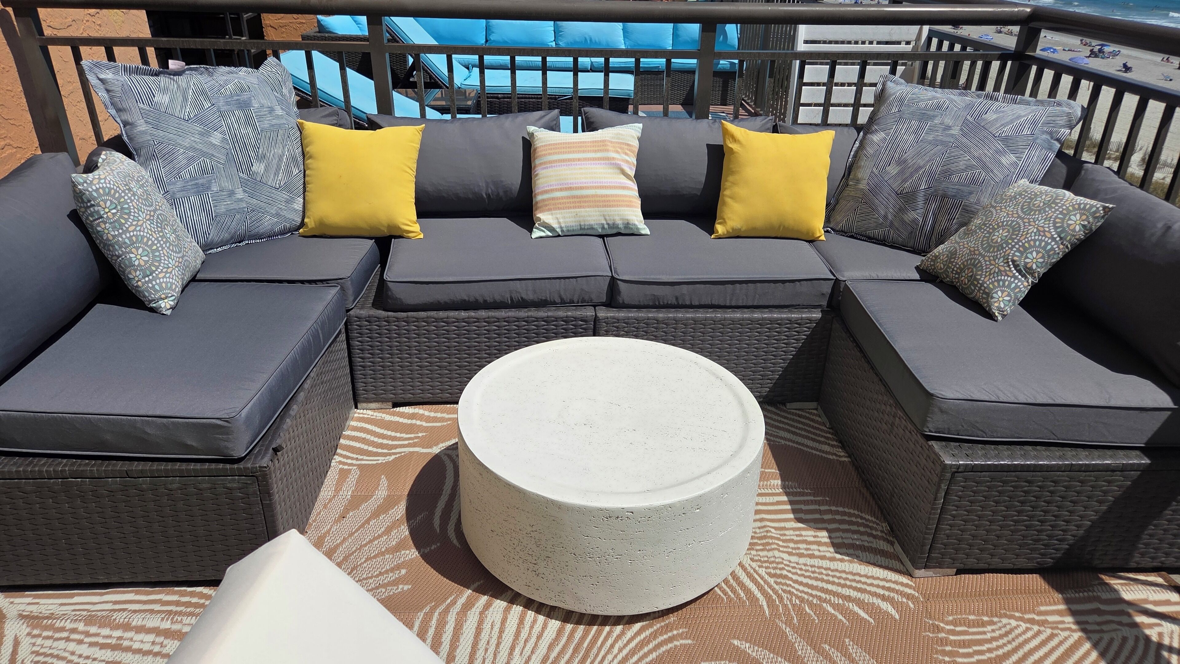 En modulsofa med mange puder og et rundt bord på en udendørs terrasse med mønster.