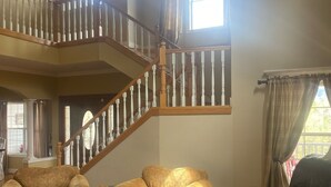 Ein geräumiges Wohnzimmer mit einer hohen Holztreppe, Ledersofas und einem großen Fenster, das natürliches Licht hereinlässt.