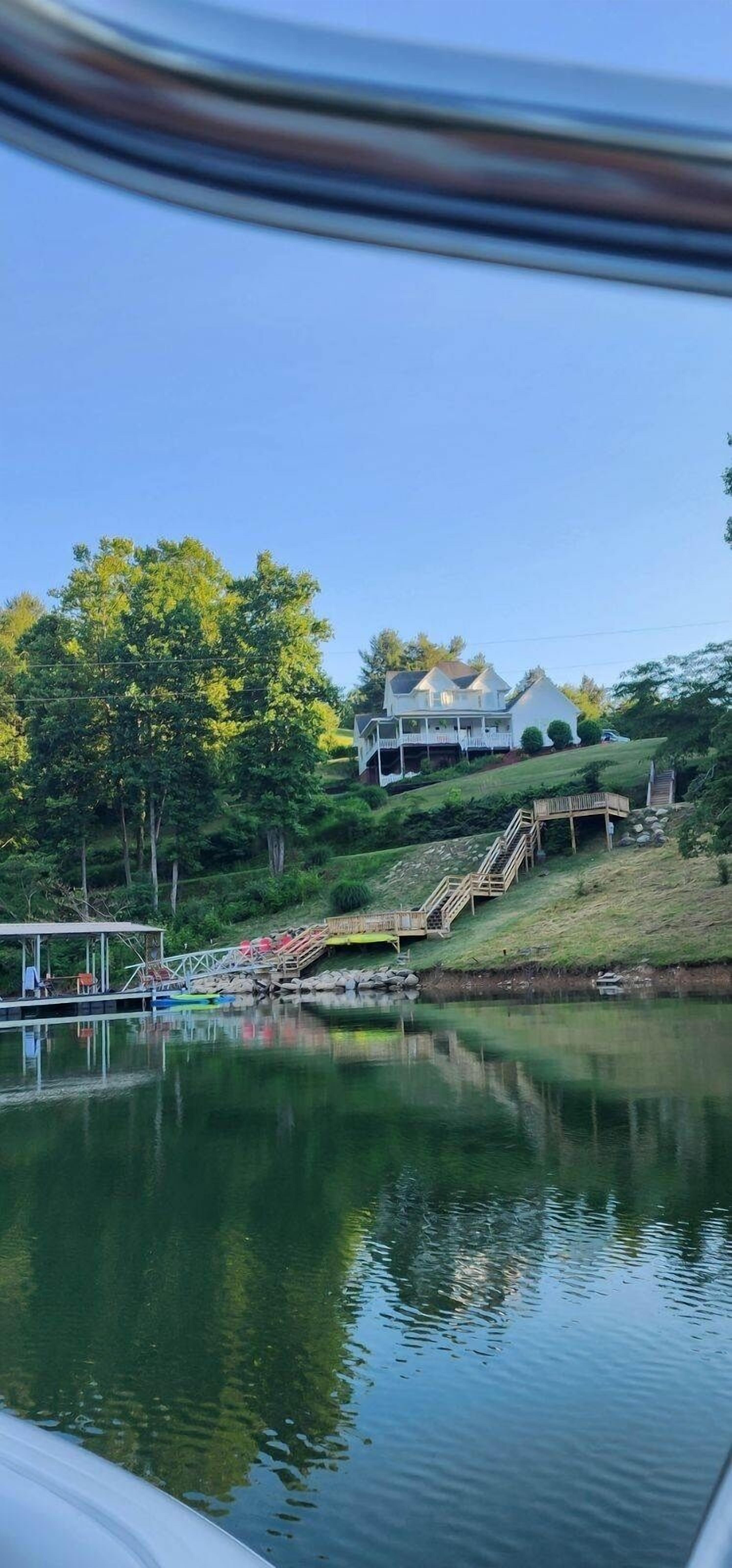 Una casa frente al lago, con un muelle, un espacio cubierto y una escalera que lleva a la casa.