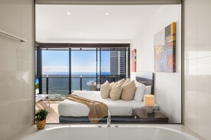 A modern bedroom with a large bed, a bedside table with a lamp, a view of the ocean, and a balcony.