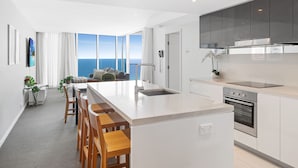 A modern kitchen with a large island, a built-in oven, and a view of the ocean. - H Residences Ocean View (Surfers Paradise)