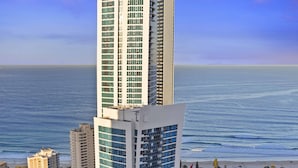 A modern hotel with a unique architectural design, featuring a prominent Hilton sign, located near a beach with a view of the ocean. - H Residences Ocean View (Surfers Paradise)