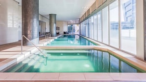 An indoor swimming pool with clear glass walls, a central column, and a staircase leading to the pool. - H Residences Ocean View (Surfers Paradise)