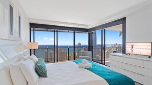 Habitación de hotel moderna con una cama grande, vistas a la ciudad y al océano, televisión y balcón con una silla.