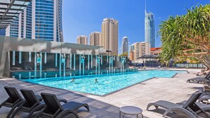 Una piscina con sillones de descanso y vistas a altos edificios al fondo.