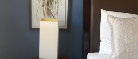 A neatly made bed with white bedding, a bedside table with a lamp, and a framed artwork of a jellyfish on the wall.
