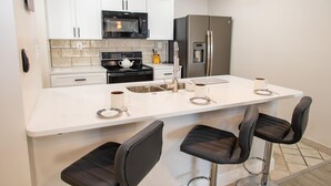 A modern kitchen with white cabinets, a black microwave, a stainless steel refrigerator, and a central island with bar stools.