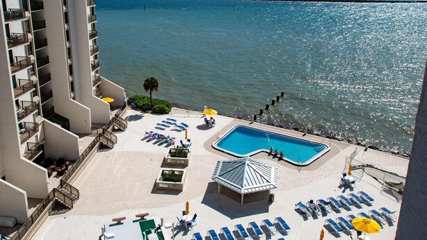 A rooftop pool area with lounge chairs and a small pool, overlooking a beach and ocean.