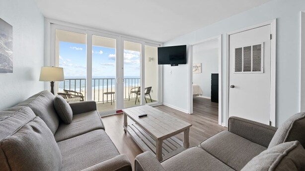 Ett modernt vardagsrum med en soffa, ett soffbord och en tv. Det finns en balkong med utsikt över havet.