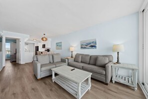 Un salon moderne avec un canapé gris, une table basse blanche et deux petites tables d’appoint avec des lampes.