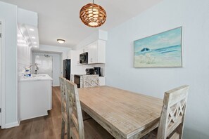 Une cuisine moderne avec des meubles blancs, une table à manger en bois et un luminaire suspendu.