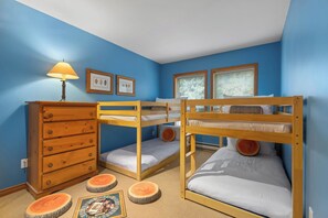 Habitación con literas, un aparador de madera, una lámpara y cuadros en la pared.