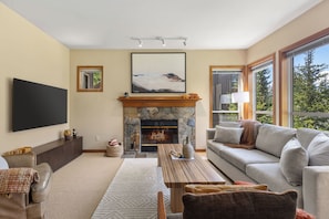 A living room with a fireplace, a sofa, a coffee table, and a TV mounted on the wall. - Popular Ski-in, Ski-out Location, Shared Hot tub (Whistler)