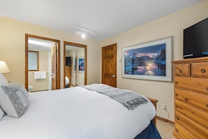 A bedroom with a large bed, a wooden dresser, a TV, and a framed picture of a lake at night. - Popular Ski-in, Ski-out Location, Shared Hot tub (Whistler)