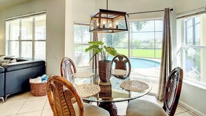 A dining area with a glass table, wicker chairs, and a hanging light fixture.