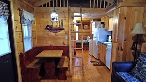 A cozy cabin interior with a wooden dining table, bench seating, a ladder, a kitchen area, and a sofa. - Bear Cabin - 2 Bedroom/1 Bath Vacation Rental (Franklin)