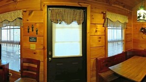 A cozy cabin interior with a wooden dining table, a television, and a kitchen area with a stove and refrigerator. - Bear Cabin - 2 Bedroom/1 Bath Vacation Rental (Franklin)