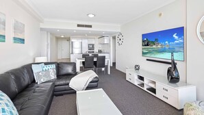 A modern living room with a black leather sofa, a white coffee table, and a flat-screen TV mounted on the wall. - Chevron Renaissance Ocean View (Surfers Paradise)