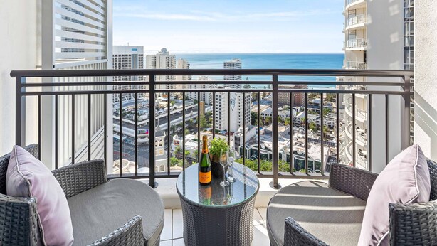 A balcony with wicker furniture, a glass table, and a bottle of champagne. - Chevron Renaissance Ocean View (Surfers Paradise)