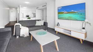 A modern living room with a grey sofa, a white coffee table, and a TV displaying a tropical beach scene. - Chevron Renaissance Ocean View (Surfers Paradise)