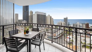 A balcony with a table and chairs, overlooking a cityscape and the ocean. - Chevron Renaissance Ocean View (Surfers Paradise)