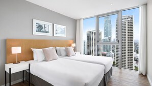 A hotel room with two beds, a wooden headboard, a nightstand with a lamp, and a large window offering a city view. - Residences H with ocean view (Surfers Paradise)