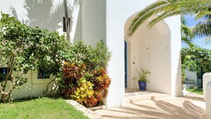 A white building with a covered entrance, surrounded by greenery and a clear blue sky. - Luxury Ocean Front Villa,  6BR (12 pax) Breakfast includes + infinity pool (Isla Mujeres)