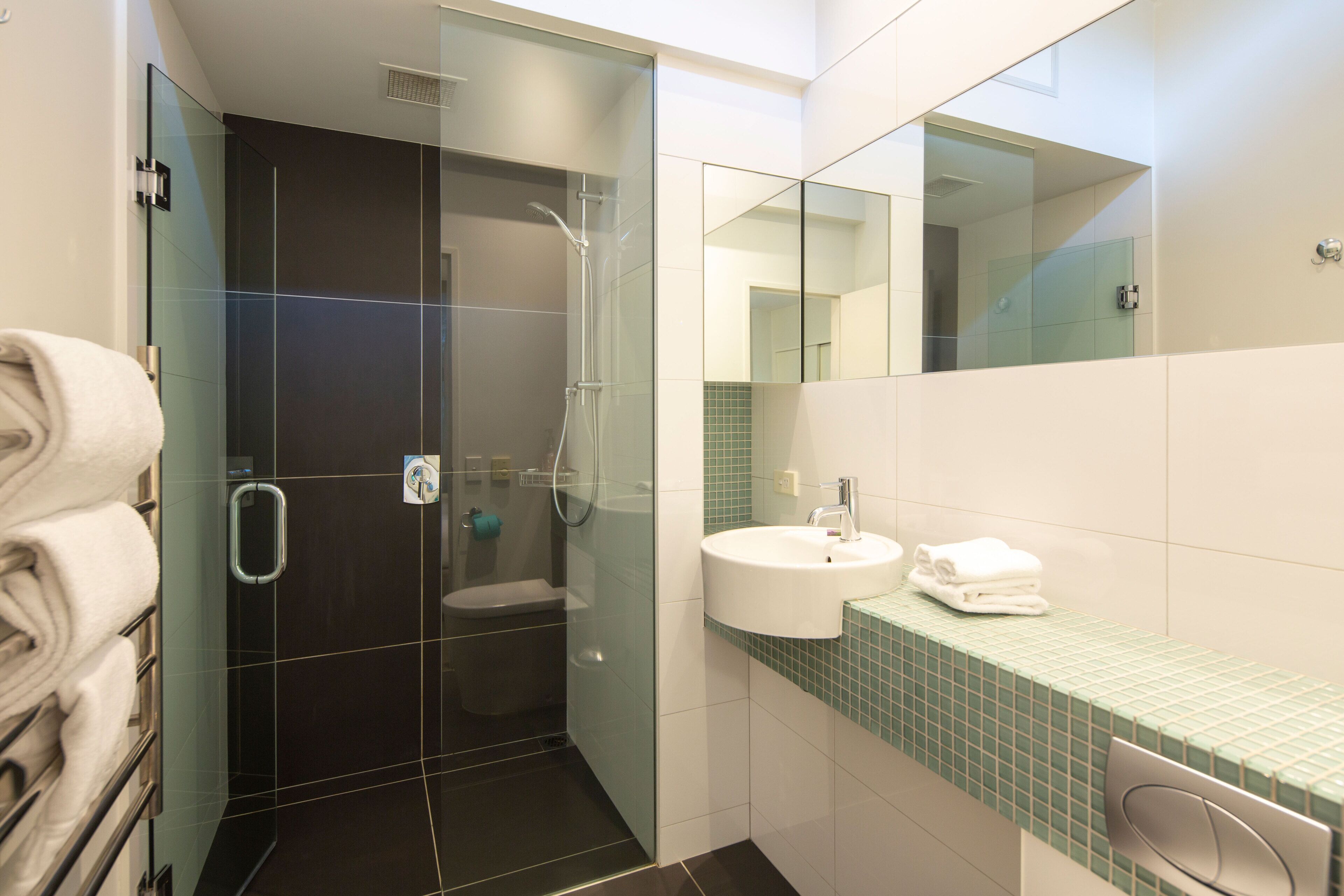 A modern bathroom with a glass-enclosed shower, a white sink, and a green-tiled countertop.