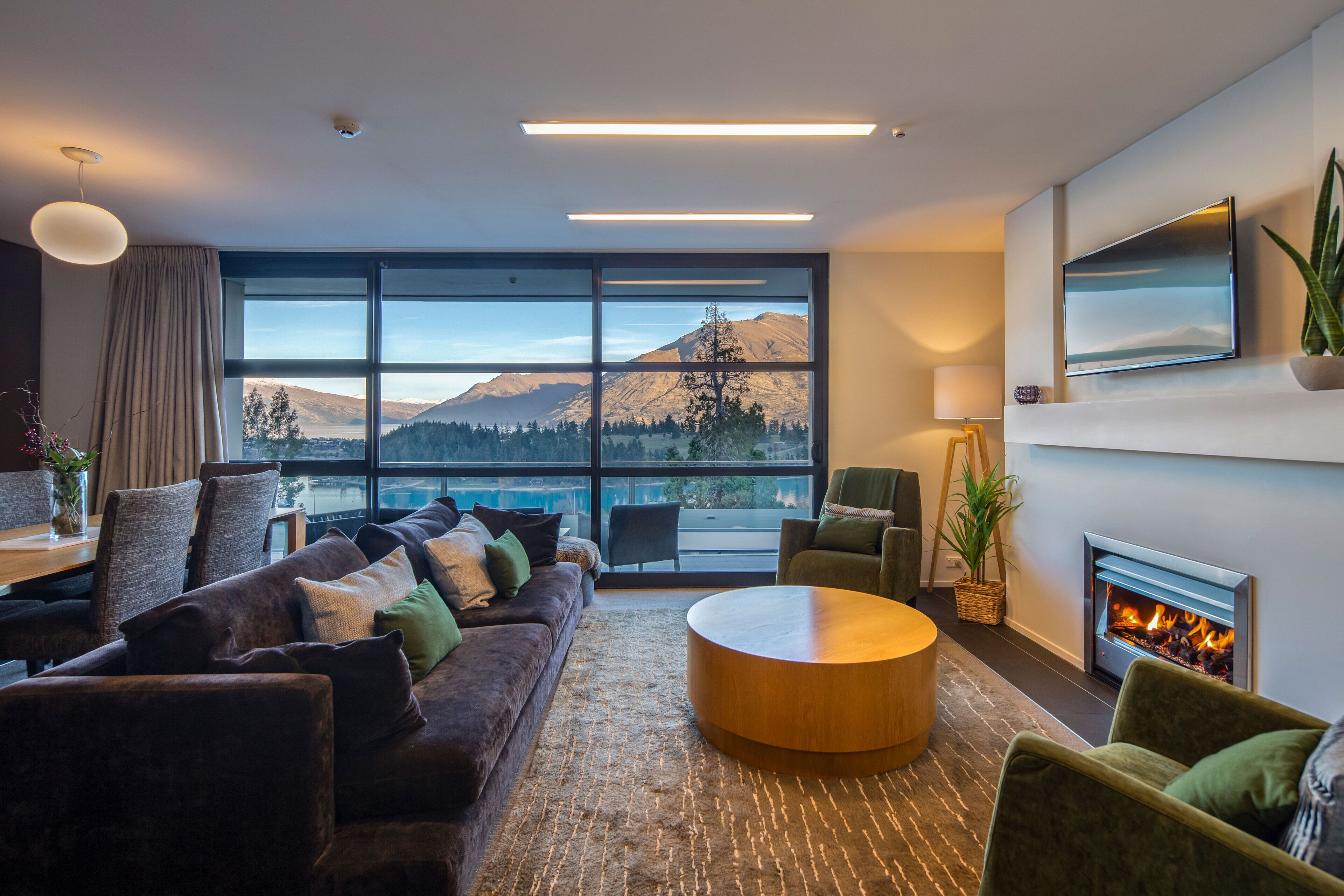 A modern living room with a large window, a fireplace, and a cozy seating area.