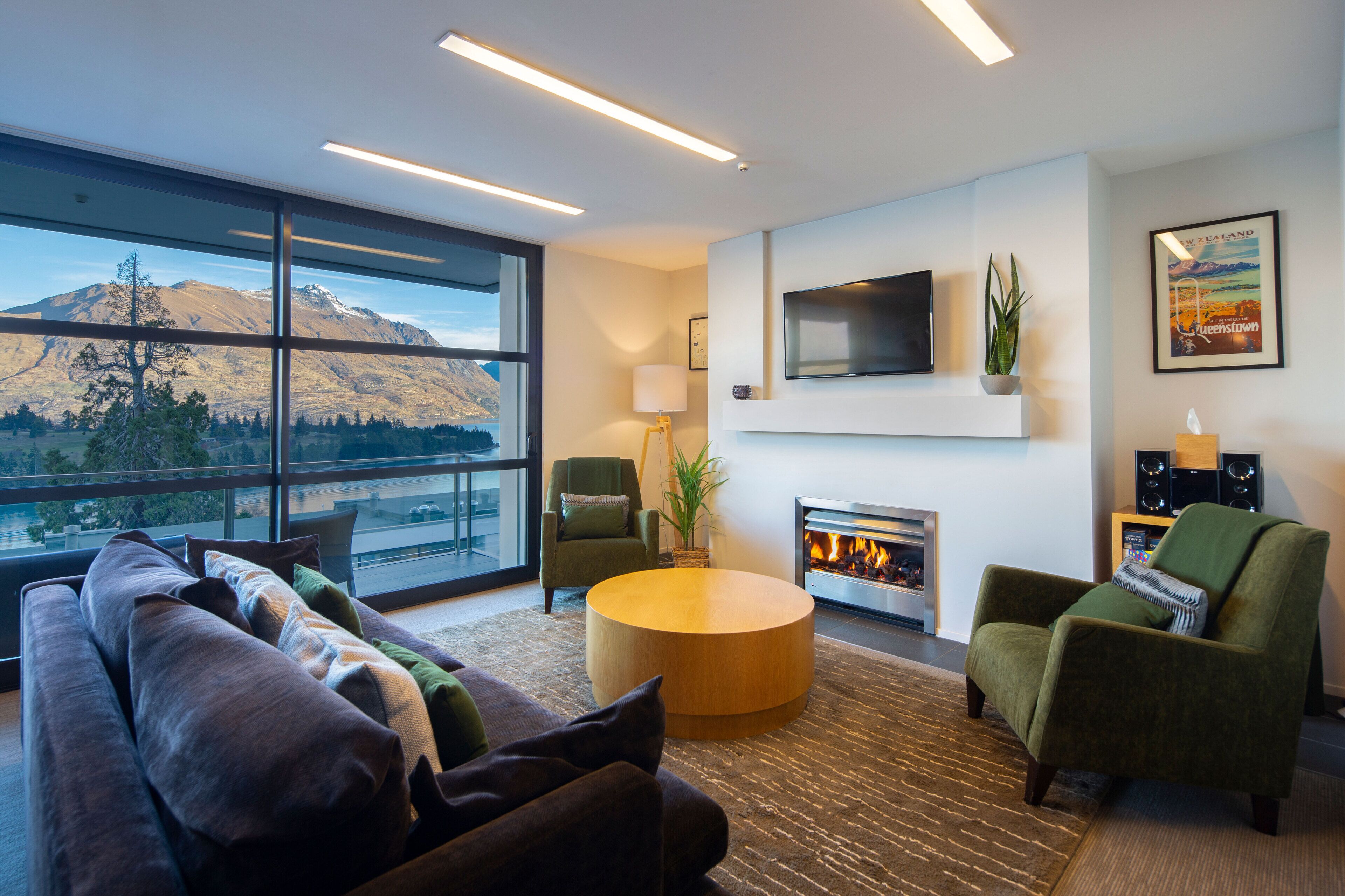 A modern living room with a large window, a fireplace, a flat-screen TV, and a cozy seating area.