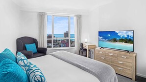 A hotel room with a bed, a desk, a chair, a TV, and a view of the ocean.