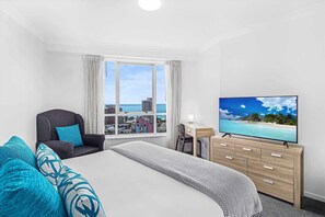 Habitación de hotel con cama, escritorio, silla, televisor y vista al océano.