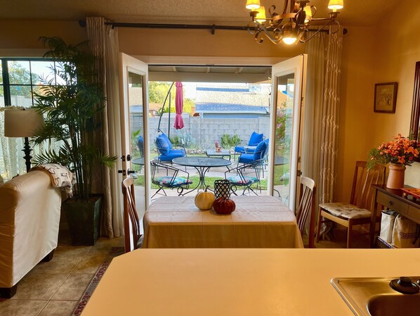 Ein Zimmer mit Esstisch und Stühlen, einer Couch, einem Kronleuchter und Blick auf eine Terrasse mit Tisch und Stühlen.