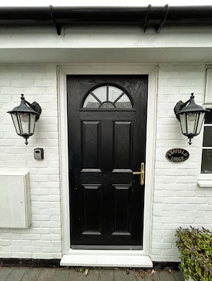 A black door with a white-framed window above it, flanked by two wall-mounted lanterns. A small plaque on the right reads "Ashfield Lodge".