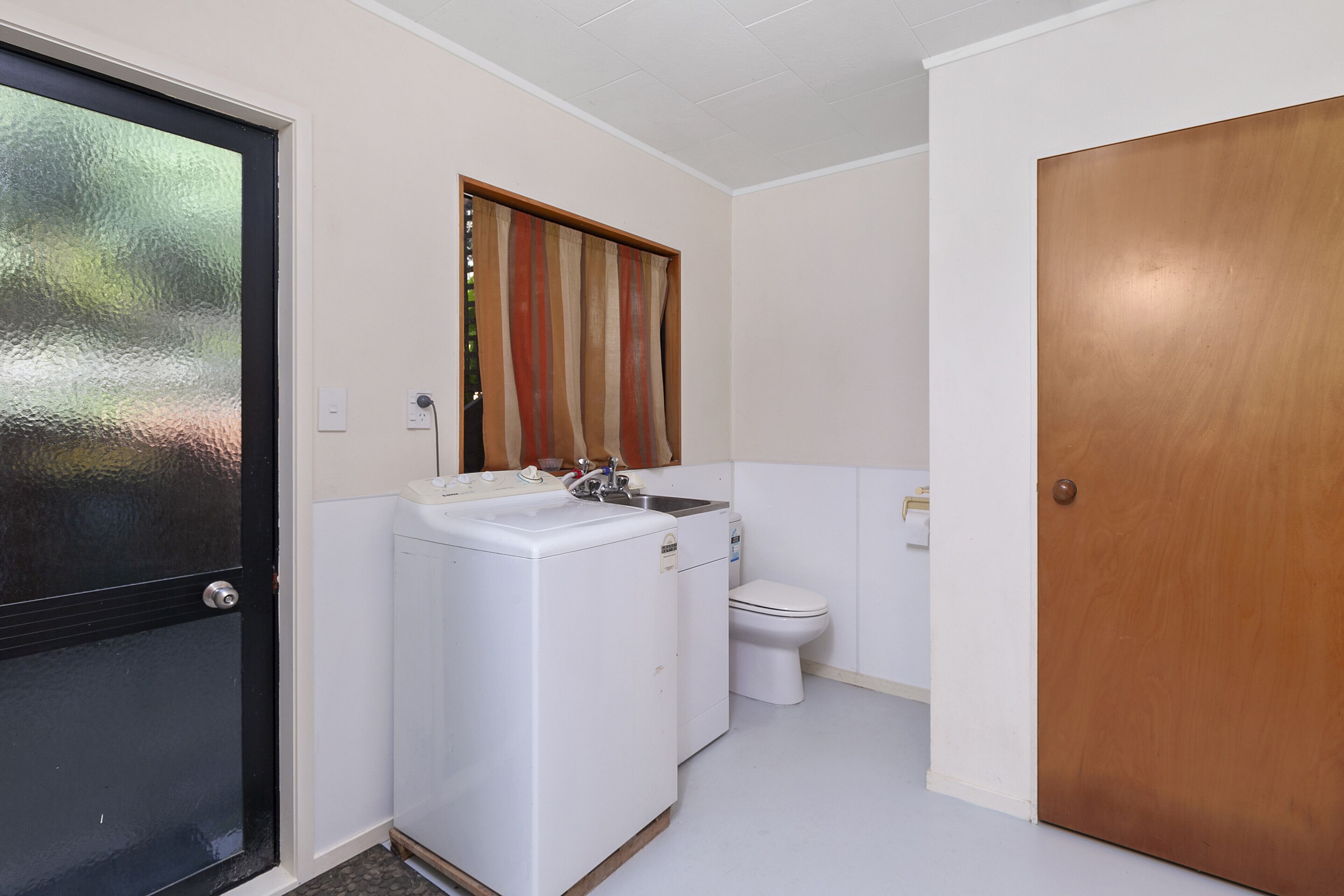 Une petite salle de bain équipée d’un lave-linge, de toilettes et d’une porte en bois.