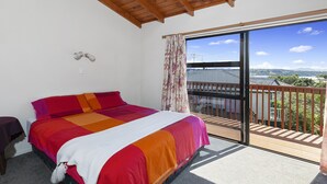 Ein Schlafzimmer mit einem großen Bett, einer Holzbalkendecke, einem Balkon mit Landschaftsblick und einer Schiebetür.