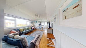 A spacious living area with a sofa set, a dining table, and a kitchen in the background.